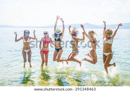 Portrait  of young group of people jumping in ocean at sunset Team of adult girl stand in water on summer beach against blue sky with clouds Water splash Hair fly in air Empty space for inscription
