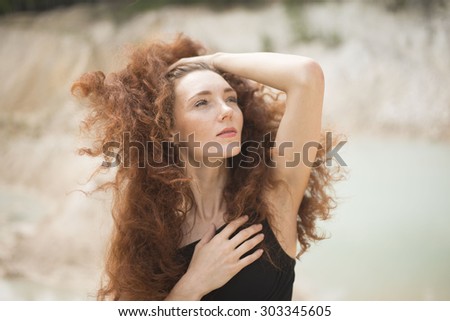 Summer sad portrait, beautiful freckled young adult girl with red hair look at camera Cute curly redhead woman with hand near face against outdoor background Empty space for inscription
