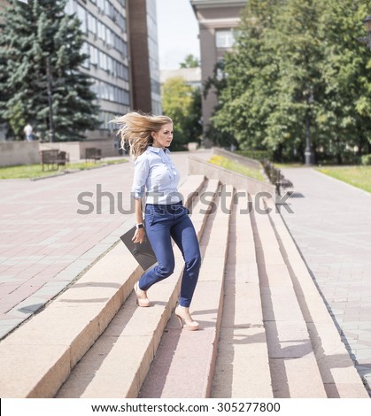 Young beautiful businesswoman go down the stairs with brief case Fast move Business lady with flying hair Shadows on stairway Girl walk on high heels against office building Summer sunny day Outdoor