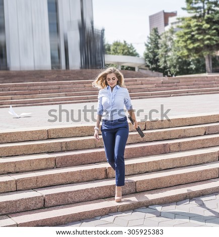 Young beautiful businesswoman go down the stairs with brief case Fast move Business lady with flying hair Shadows on stairway Girl walk on high heels against office building Summer sunny day Outdoor
