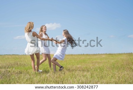 Three girlfriend reel  round circling in dance in the summer daisy summer field against blue sky with white clouds. 3 caucasian woman play outdoor in short stylish dress Empty space for inscription