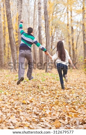 Back view of Young adult latin hispanic couple running in morning in dry autumn park Empty Copy Space for inscription. Hands up. Man and woman run in fall forest. Rear view