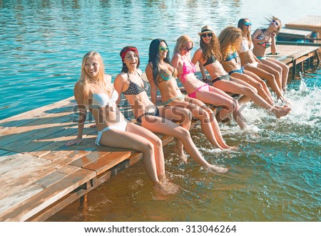group of happy young woman feet splash water in sea and spraying at the beach on beautiful summer sunset light. Eight sexy girls playing on wooden pontoon against blue sky background Enjoy holiday