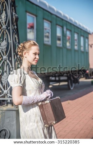 Young adult woman standing near old retro vintage train Caucasian girl under street light Cute slim female waiting wagon with luggage Elegant Lady wear long white dress