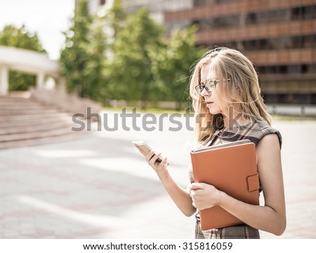 Young business woman using cell mobile phone and hold in hand digital tablet computer or case with documents Businesswoman stand alone against office building on street near stairway