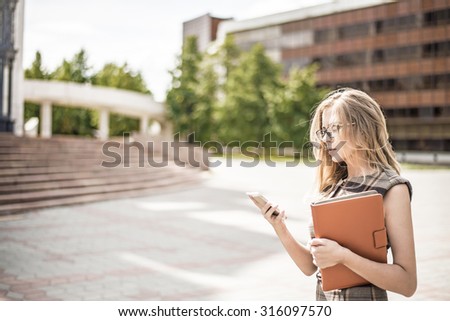 Young business woman using cell mobile phone and hold in hand digital tablet computer or case with documents Businesswoman stand alone against office building on street near stairway