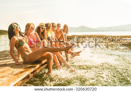 group of happy young woman and man feet splash water in sea. Spray at  beach on beautiful summer sunset light. Six sexy girls and gay play on wooden pontoon against blue sky background Enjoy holiday