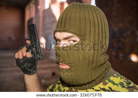 Close-up of serious armed criminal with black metal gun Russian policeman in camouflage mask with pistol. Green mask on head Inside building Look at camera