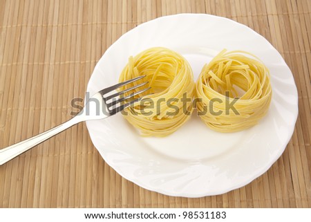 portion of spaghetti in a plate with fork on bamboo background