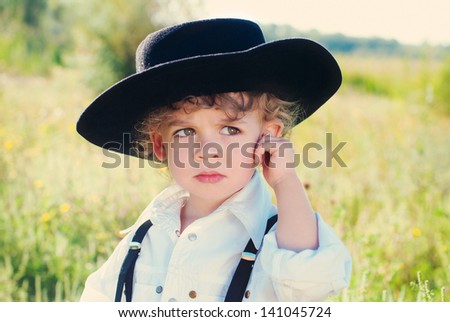 Glamorous little boy in a hat outdoors. Conceptual idea.