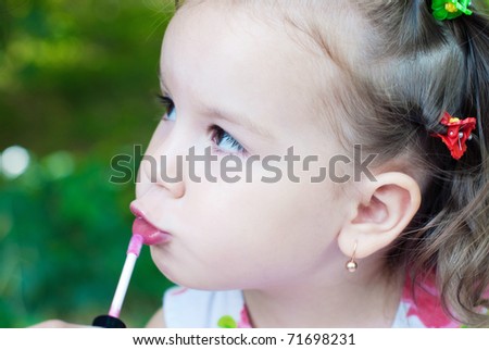 The little girl paints lips with lipstick