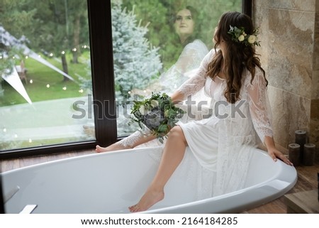 Lush, adorable bride in the bathroom by the mirror and white tub. Stylish girl in a wedding dress with a bridal bouquet. Photo stock © 