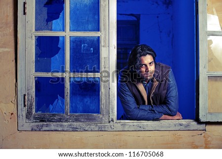 Smart Indian young man looking through window.