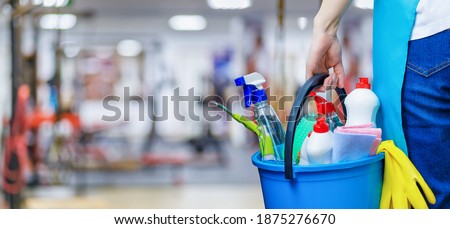 The concept of cleaning the fitness room. Cleaning lady with a bucket of cleaning products stands against the background of the fitness room.