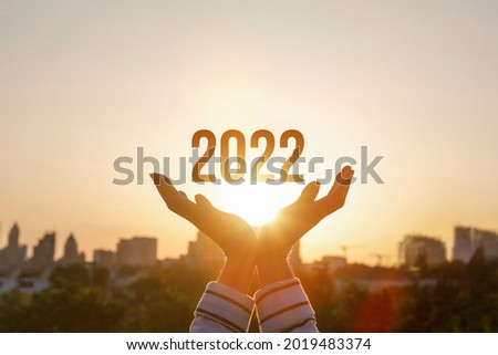 2022 is supported by woman hands on the background of a sunny sunset.