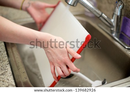 Woman washes cutting board in kitchen sink
