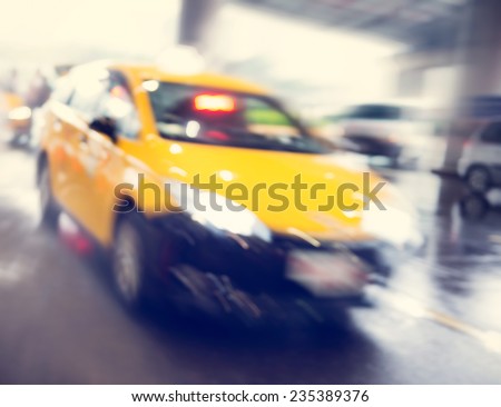 Bright yellow iconic taxi cab speeding past the illuminated entrance of an airport terminus building with motion blur of the car