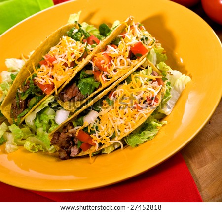 A plate of freshly prepared ground beef tacos, with tomato, freshly grated cheese, lettuce and sour cream.
