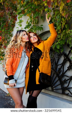 Outdoor lifestyle fashion close up portrait of two pretty cheerful girls friends, smiling and having  fun. Walking on the autumn city. Wearing stylish bright outerwear with handbags and sunglasses.