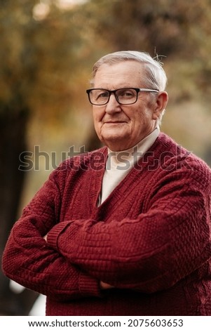 Handsome and plump elderly man in an elegant cap, scarf and red sweater posing, standing under a beautiful tree with golden leaves in an autumn park, resting and enjoying the bright foliage, happy ret Stok fotoğraf © 