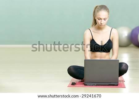 The beautiful girl sits with the laptop in sports hall