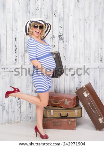 Stylish pregnant lady tourist with suitcases near wooden wall