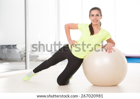 She make exercise with pilates ball on floor. Beautiful sporty woman posing for camera in sport gym.