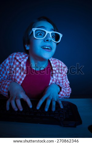 Little boy look to computer display. He like play and win video games. In blue light of display emotional kid play computer games online.