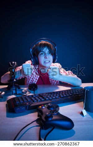 He is going to revenge to another player. He like play and win video games. In blue light of display emotional kid play computer games online.