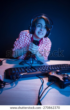 Young gamer like to play video games. In blue light of display kid play computer games online.