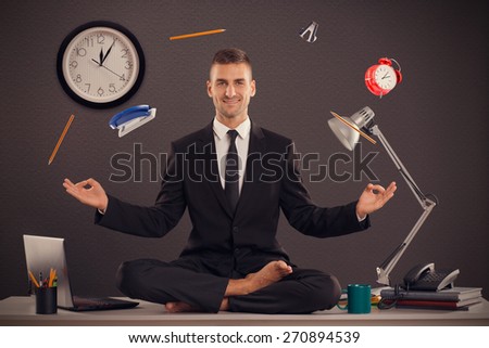 He is businessman that can relax in office, while his work is doing. Handsome businessman sit on table in office in lotus position and try to relax.