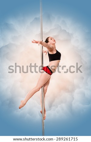 Pretty pole dancer posing in studio. Young sexy girl practicing with her arms extended sidewards isolated on blue.