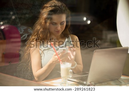 Sexy girl reading messages on phone. Freelancer working in restaurant with laptop.
