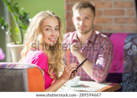 First date with telephone in her hands. Sexy girl in pink T-shirt smiling and resting with boyfrient in cafe.