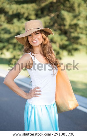 Photo of pretty young woman smiling along the road. Girl with fashionable bag standing with her arm akimbo.