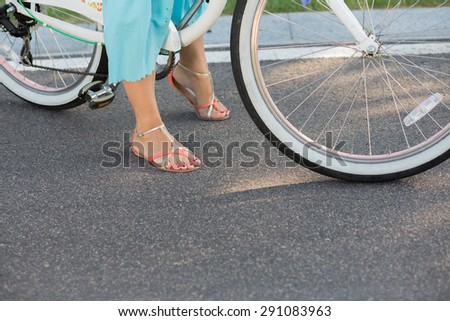 Legs of summer girl with bicycle. Two-wheeled white bicycle id kept by pretty girl in blue skirt.