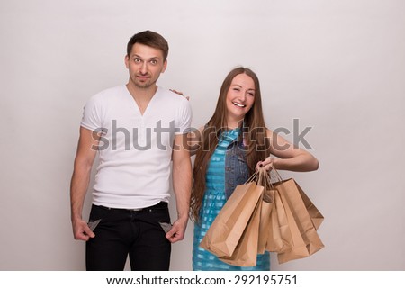 Man in white T-shirt is bankrupt. Girl keeping packages in her hands full of clothes abd accessories after shopping.
