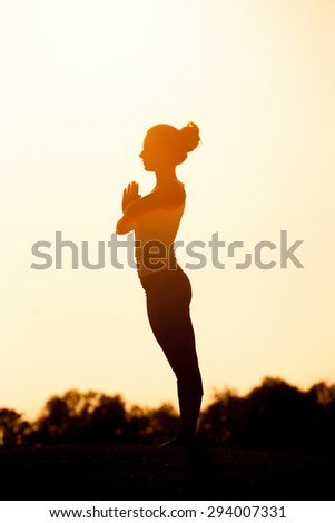 Black  silhouette of yogi girl with her hands clasped on her chest. Beautiful girl with ideal back posture practicing.
