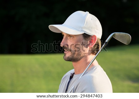 Golf player posing with golf club. Training of handsome mature man on green sunny course.