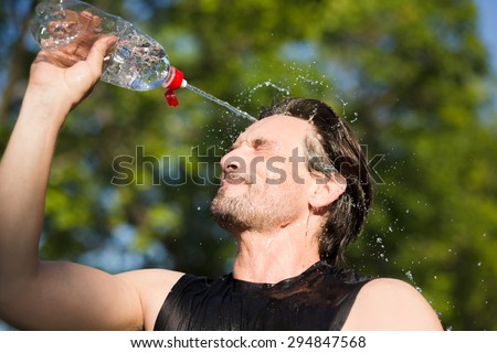Fitness runner drinking and splashing water in his face. Funny image of handsome male refreshing during workout.