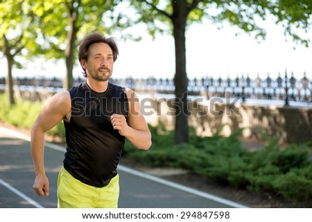 A shot of a mixed race man running outdoors. Man in black  sleeveless sports shirt training in the park.