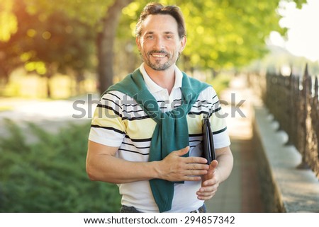 Portrait of handsome young man smiling outdoor. Rich guy in fashionable T-shirt demonstrating healthy life style on nature.