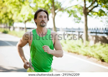 Handsome man jogging. Healthy looking young man jogging in the park under morning sunlight.