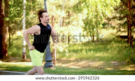 Handsome man running in the forest at sunrise. Male fit sport fitness model training for marathon outside in beautiful landscape.