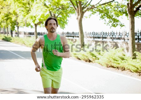 Athletic man running in the park. Asian runner jogging outdoors with tree\'s in background.