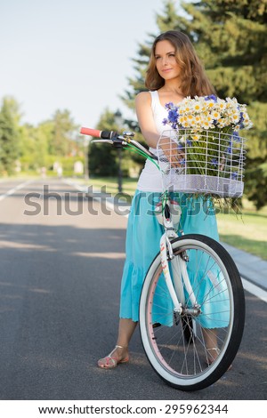 Summer girl posing with bicycle on the road. Beatiful girl with long brown hair in summer clothes smiling for the camera.