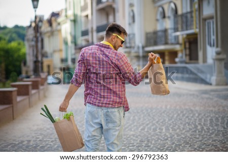 Portrait of young man's back in sunglasses. Handsome man lifting bag full of food with his right hand.