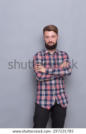 Hipster bearded man happy posing isolated on grey. Man in hipster plaid shirt standing with his arms crossed.