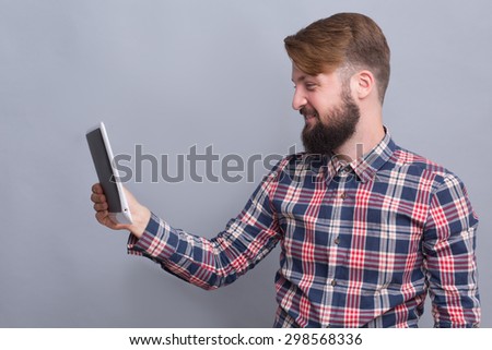 Hipster bearded man having video communication on tablet PC. Man with up-to-date haircut smiling for the camera and speaking with friends.