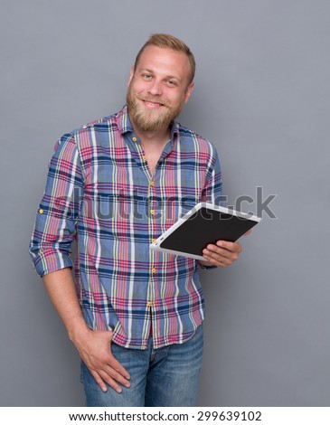 Close-up portrait of smiling bearded man with tablet PC. Blond man in plaid shirt and jeans looking at the camera with pleasure.